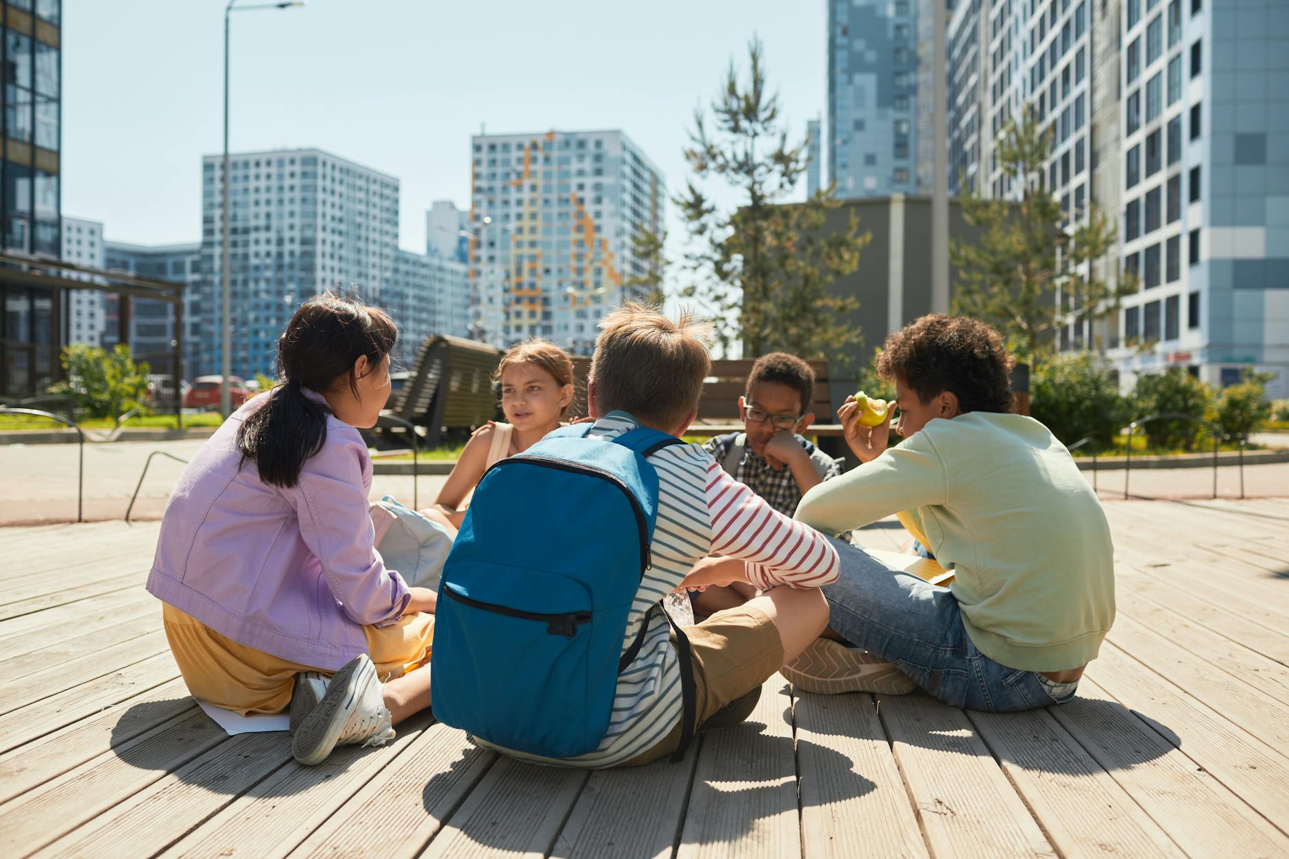 group of schoolkids sitting outside in sunlight in city